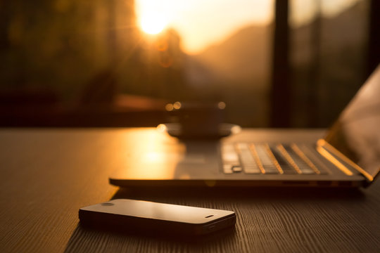 Computer Coffee Mug and Telephone on black wood table sun rising