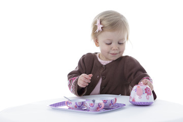 toddler girl playing with tea set, holding tea pot, isolated on white background