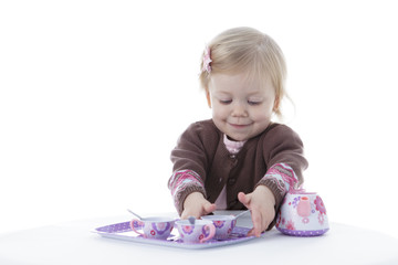 toddler girl playing with tea set, reaching out for cup, isolated on white background