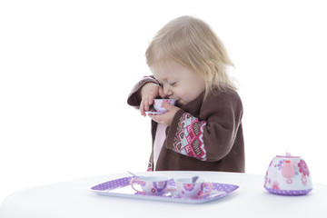 toddler girl playing with tea set, sipping tea, isolated on white background