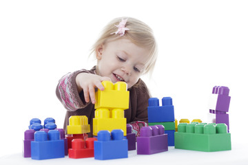 toddler girl playing with building blocks, reaching out for cup, isolated on white background