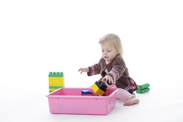 toddler girl picking up toys in pink bin, isolated on white background