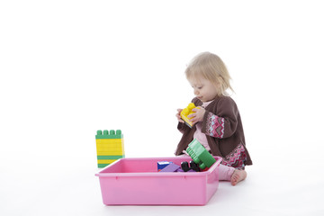 toddler girl picking up toys in pink bin, isolated on white background