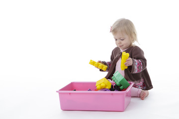 toddler girl picking up toys in pink bin, isolated on white background