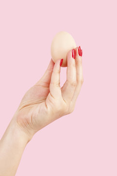 Female hand with red fingernails holding two eggs.