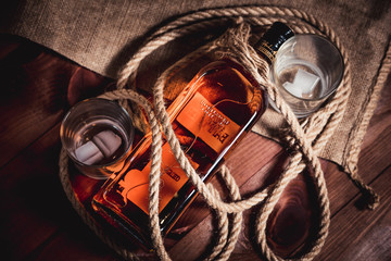 Whisky glass with ice, a bottle of whiskey and a rope