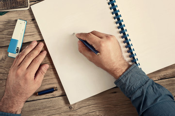 Men writes in an open notebook with blank pages on wooden desk c