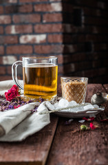 cup of black tea with sugar cane, roses, tea leaves on a brown wooden background