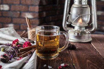 cup of black tea with kerosene lamp, sugar cane, roses, tea leaves on a brown wooden background