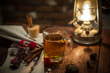 cup of black tea with kerosene lamp, sugar cane, roses, tea leaves on a brown wooden background