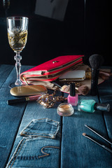 Fototapeta na wymiar female handbag with cosmetics and glass of champagne on jeans background