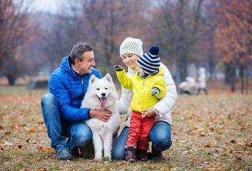 Fototapeta premium Happy family playing with samoyed dog in autumn park
