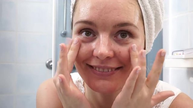 Woman in towel on head with no makeup making face massage 4K