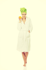 Spa woman in bathrobe holding orange.