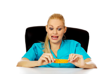 Shocked and scared female nurse or doctor sitting behind the desk and holding packet of pills