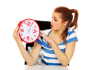 Young shocked teenage woman looking at clock