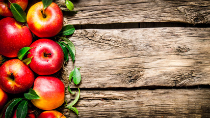 Fresh red apples with green leaves on wooden table.