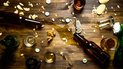 In the process of party - spilled beer, bottle caps and leftover chips on the table. - obrazy, fototapety, plakaty