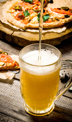 The breath of fresh beer being poured into glass. On the background of the pizza.