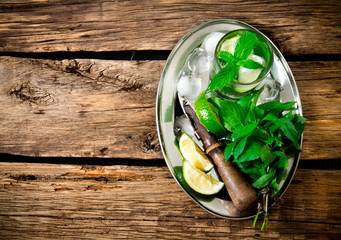 Fresh cocktail of lime, mint, rum and ice on a metal tray . On a wooden table. Free space for text .