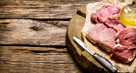 Fresh raw meat with knife and oil on a wooden stand.
