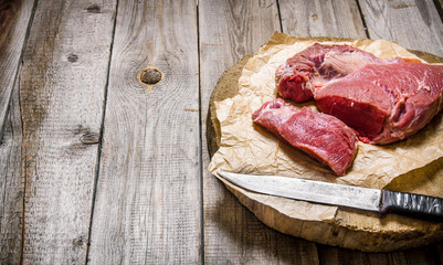 Cutting raw meat a large knife. On wooden table.