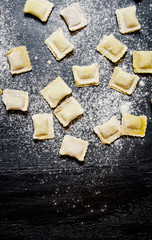 Homemade ravioli with flour. On black table with flour.