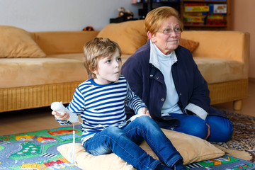 Little kid boy and grandmother playing video game console