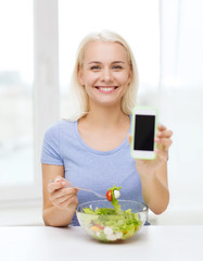 smiling woman with smartphone eating salad at home