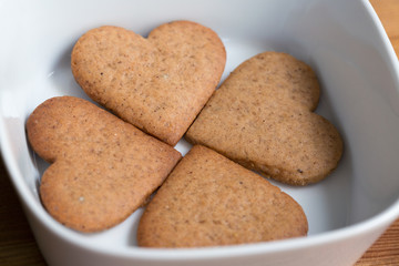 A white bowl with four heart shaped homemade cookies on wooden background