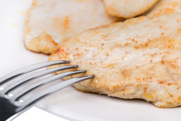 Fried chicken meat on a plate. With a fork, close-up.