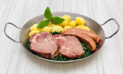 Grünkohlpfanne mit Kasseler und Kohlwurst auf weißem Holzunter