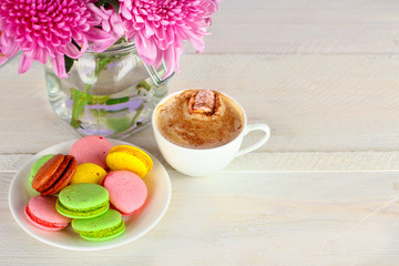Obraz na płótnie Canvas Colorful delicious macaroons on a plate and a Cup of coffee on a wooden table with flowers in a jar of water