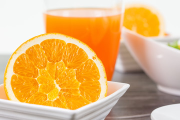 Eine halbe Orange in weisser Schale. Hintergrund ein Glas Orangensaft. Auf dunklem Holz.