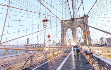 People crossing Brooklyn Bridge at sunset