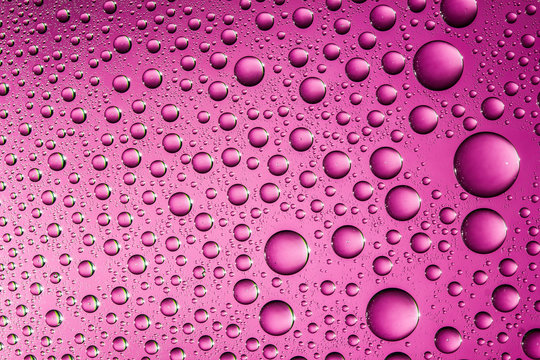 Pink water drops on glass surface texture.