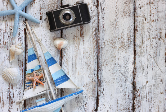 top view image of photo camera, wood boat, sea shells and star fish over wooden table
