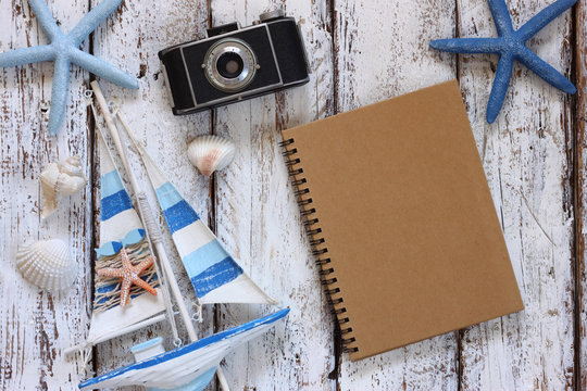 top view image of blank notebook, wooden sailboat, starfish, shells and camera. travel and adventure concept
