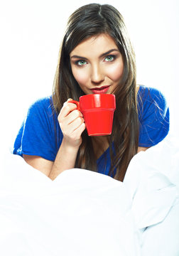 Woman sitting in bed with red coffee cup.