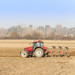 Obraz premium Red Tractor Plowing in Autumn.