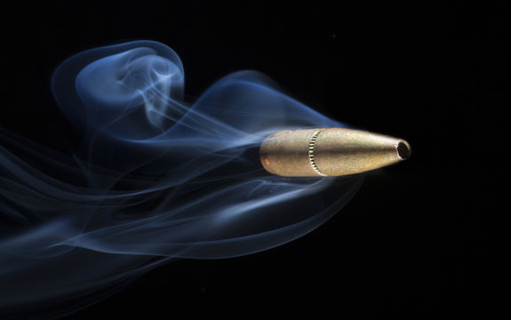 Copper bullet speeding across a dark background with smoke flowing behind 