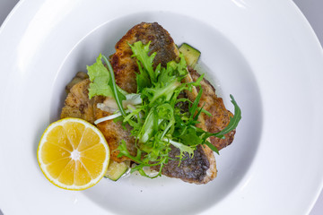 Cooked dorado fish with vegetables and lemon in white plate