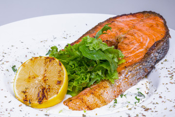 Grilled salmon steak with spinach in white plate, top view