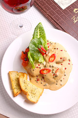 beef with pepper sauce on a white plate with croutons and salad leaves