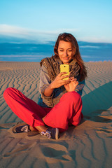 Young woman sitting on the sand in the desert and is looking at the phone