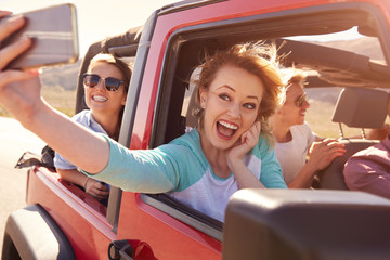 Friends On Road Trip In Convertible Car Taking Selfie