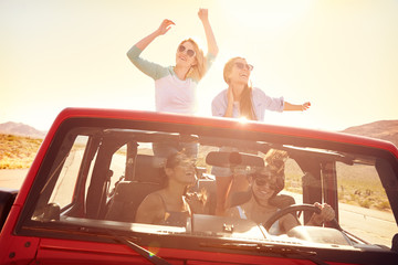 Four Female Friends On Road Trip Standing In Convertible Car