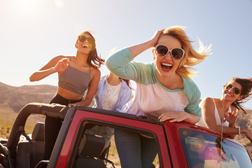 Four Female Friends On Road Trip Standing In Convertible Car