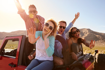 Friends On Road Trip Standing In Convertible Car