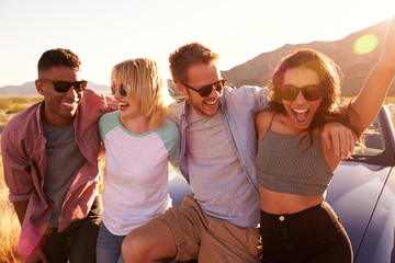 Friends On Road Trip Sitting On Hood Of Convertible Car